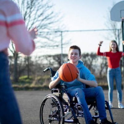 Teenage Boy In Wheelchair Playing Basketball With Friends
